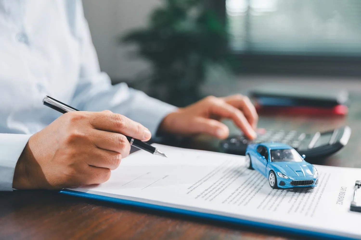 Hand signing an auto insurance form beside a small blue model car